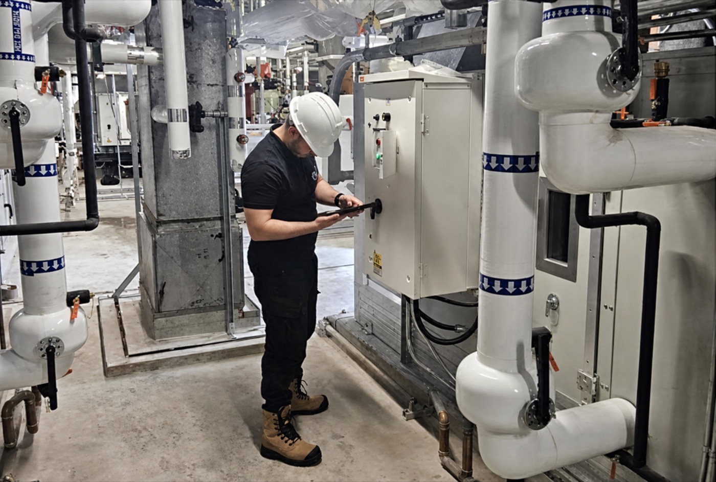Technician checking mechanical equipment in a plant room